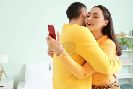 Téléchargez les photos : Young woman with mobile phone hugging her husband at home. Cheating concept - en image libre de droit