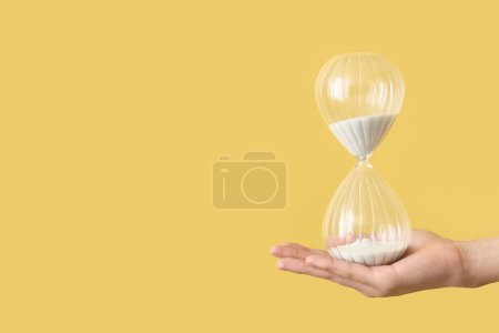 Female hand holding hourglass on yellow background
