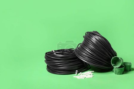 Rolled cables, wall plugs and socket mounting boxes on green background