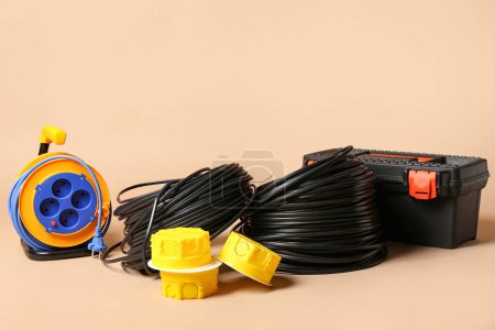 Electrical junction boxes, rolled wires, tool box and extension cable reel on beige background, closeup