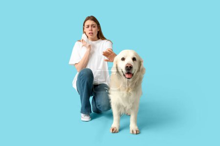 Mujer joven que sufre de alergia a las mascotas con perro labrador sobre fondo azul