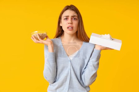 Young woman with tissue box and bowl with nuts suffering from allergy on yellow background