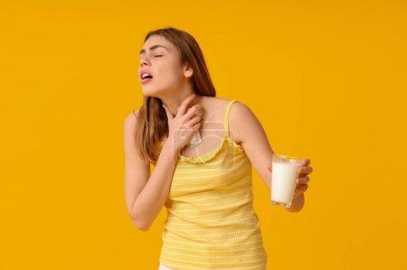 Woman with tissue and glass of milk suffering from allergy on yellow background
