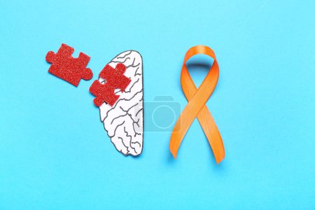 Papierhirn mit Puzzleteilen und orangefarbenem Band auf blauem Hintergrund. Multiple Sklerose: Monat des Bewusstseins