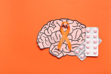 Papierhirn mit Pillen und orangefarbenem Band auf farbigem Hintergrund. Multiple Sklerose: Monat des Bewusstseins