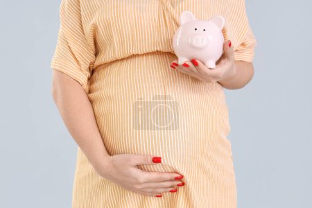 Young pregnant woman with piggy bank on light background, closeup. Maternity Benefit concept