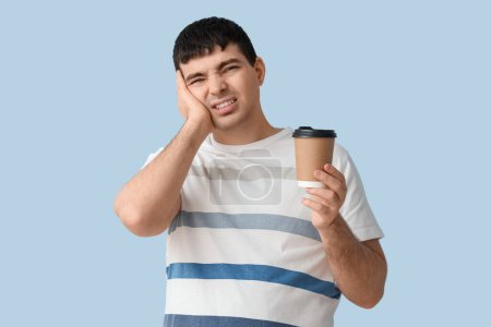 Junger Mann mit Kaffeetasse leidet unter Zahnschmerzen auf blauem Hintergrund