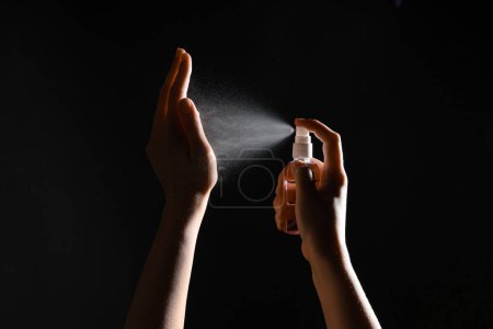 Woman applying sanitizer on her hands against black background
