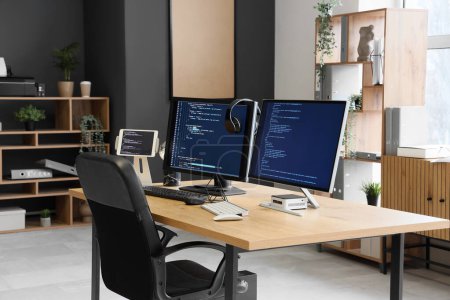 Computermonitore mit Programmiercode und Kopfhörer auf dem Schreibtisch im Büro