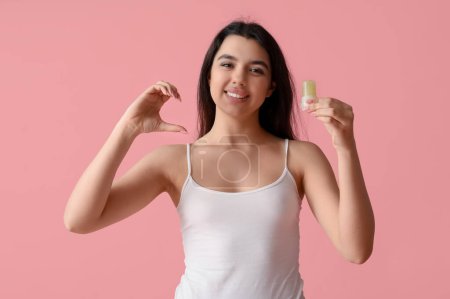 Happy smiling young woman holding crystal deodorant and making heart with her hand on pink background