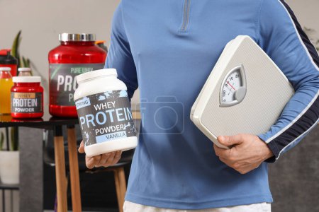 Téléchargez les photos : Jeune homme sportif avec poudre de protéines et balances de poids dans la cuisine, gros plan - en image libre de droit