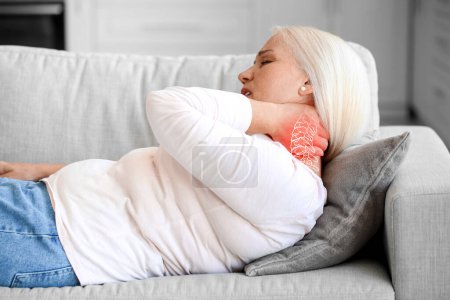 Ältere Frau leidet unter Nackenschmerzen, während sie zu Hause auf dem Sofa liegt