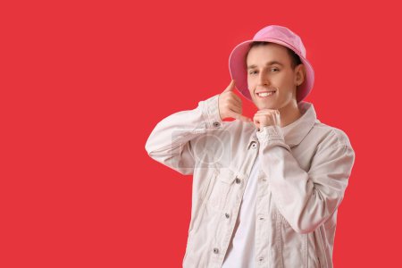 Cool young man showing "call me" gesture on red background
