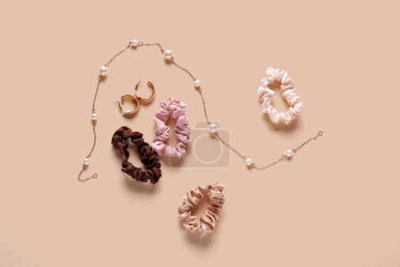 Silk scrunchies with earrings and necklace on beige background