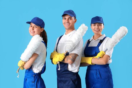 Workers of cleaning service with pp-dusters on blue background
