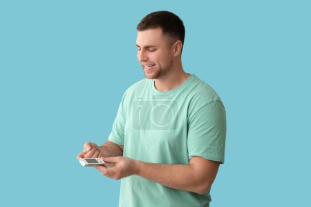 Handsome young happy diabetic man checking blood sugar level on blue background