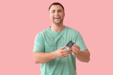 Handsome young happy diabetic man with glucometer on pink background