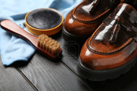 Glänzende Lederschuhe, Stoff, Pinsel und Schuhcreme auf schwarzem Holzhintergrund