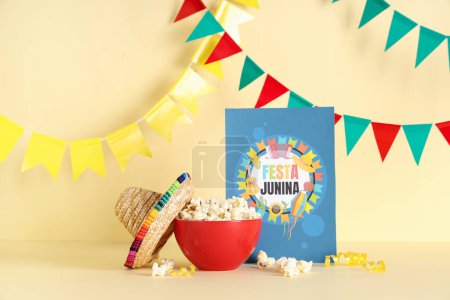 Foto de Cuenco de palomitas de maíz sabrosas, mini sombrero, tarjeta de felicitación y banderas para la celebración de Festa Junina en el fondo de color - Imagen libre de derechos