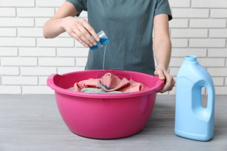 Woman adding laundry detergent to clothes in plastic basin on grey grunge table