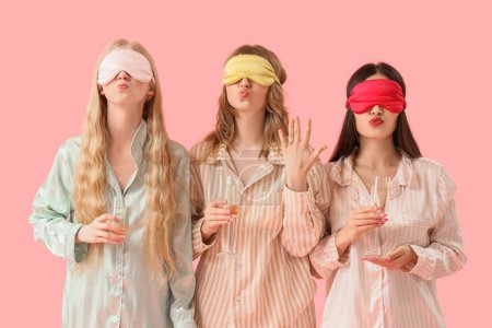Young woman and her bridesmaids in pajamas with champagne blowing kisses on pink background. Hen Party