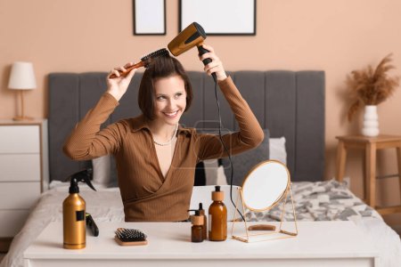 Schöne junge glückliche Frau mit Haartrockner, Bürste und Haarpflegeprodukten zu Hause