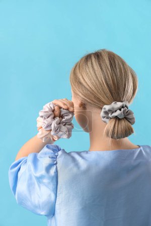 Young blonde woman with scrunchies on blue background, back view
