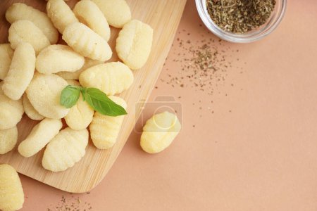 Wooden board with tasty gnocchi and spices on beige background