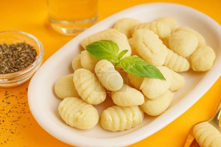 Plate with tasty gnocchi and spices on orange background, closeup