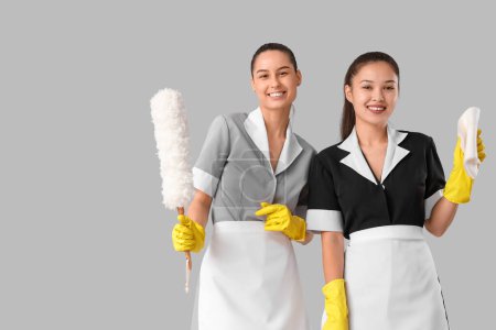 Camareras jóvenes con artículos de limpieza sobre fondo claro
