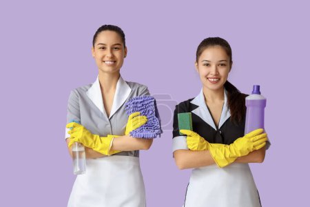 Camareras jóvenes con artículos de limpieza sobre fondo lila