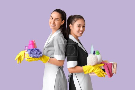Camareras jóvenes con artículos de limpieza sobre fondo lila