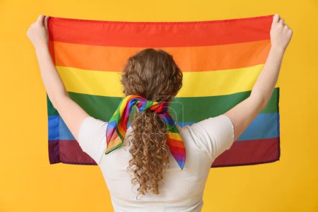 Young woman with LGBT flag and hairscarf on yellow background, back view