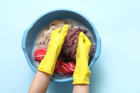 Woman in rubber gloves washing clothes in plastic basin on blue background