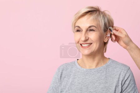 Mujer joven poniendo audífono en el oído de la mujer madura sobre fondo rosa