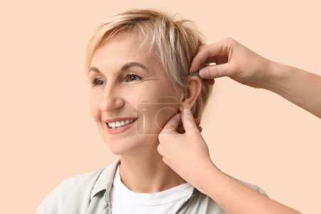 Mujer joven poniendo audífono en el oído de la mujer madura sobre fondo beige