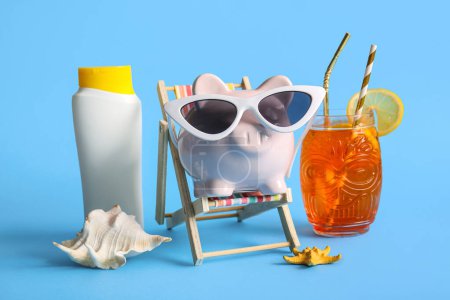 Piggy bank in sunglasses, seashells, sunscreen, cocktail and decorative deckchair on blue background
