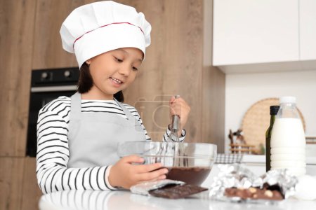 Lustige kleine asiatische Mädchen Whisking geschmolzene Schokolade in der Küche