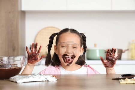 Lustige kleine asiatische Mädchen mit Schokolade auf ihren Händen zu Hause