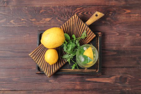 Boards with glass of fresh mint tea and lemons on brown wooden background
