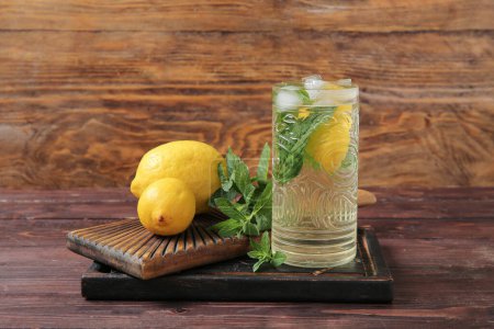 Boards with glass of fresh mint tea and lemons on brown wooden table