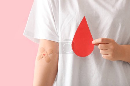Donateur avec patchs médicaux appliqués et goutte de sang en papier sur fond rose, gros plan