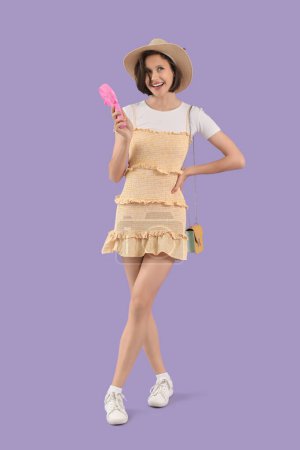 Mujer joven con ventilador eléctrico pequeño rosa sobre fondo lila