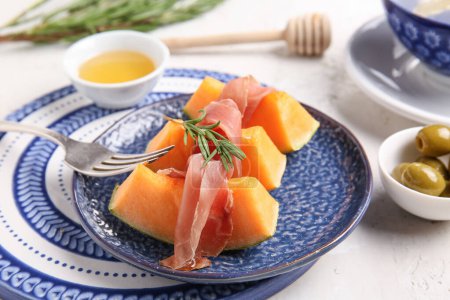 Plate with tasty melon, prosciutto and honey on light background, closeup