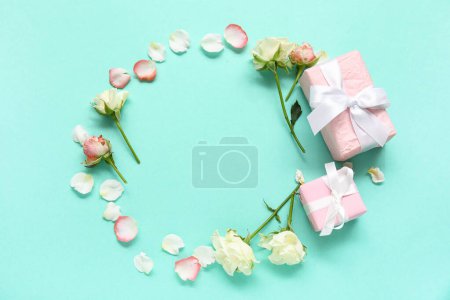 Frame made of gift boxes with roses and petals on turquoise background