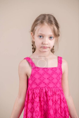 Portrait of a cute little girl in a pink dress on a beige background