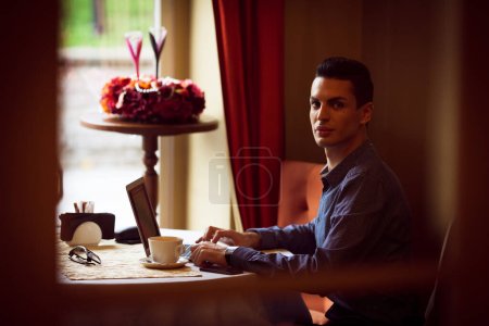 Téléchargez les photos : Concept de style de vie communautaire LGBTQ. Jeune homme homosexuel assis à la table dans un café de la ville à l'ancienne. Beau gay homme d'affaires travaille sur ordinateur portable tout en ayant une pause au déjeuner. - en image libre de droit