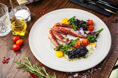 Photo for Octopus with black risotto. Carrot cream, mini-broccoli, basil pesto. Delicious healthy traditional food closeup served for lunch in modern gourmet cuisine restaurant. - Royalty Free Image
