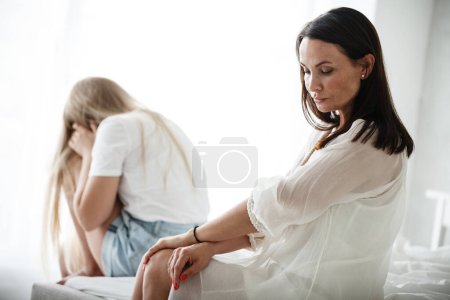 Photo for Family conflict and relations concept. Mother and daughter having quarrel and aguring at home. Sad woman and teenage girl sitting on bed. Not looking at each other. - Royalty Free Image