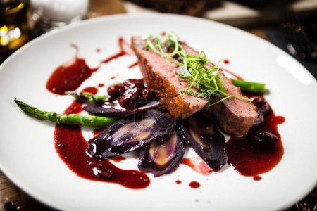Photo for Duck breast with asparagus, purple carrot, demi-glace amd cherry sauce. Delicious healthy grilled and roasted bird fillet food closeup served on a table for lunch in modern cuisine gourmet restaurant. - Royalty Free Image